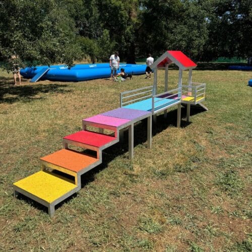 Aire de jeux petite race vue de l'escalier multicolore menant à la passerelle et à la rampe verte
